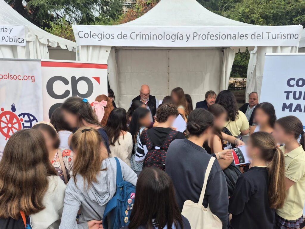 Decenas de estudiantes ante la carpa de los Colegios de Criminología y Profesionales del Turismo, con el cartel del CPCM a la izquierda, en el Real Jardín Botánico Alfonso XIII.