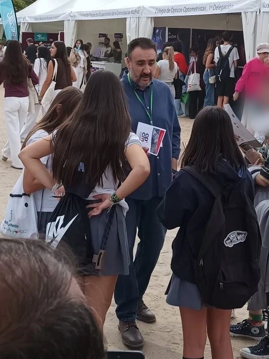 Un representante del Colegio, con un folleto del CPCM en la mano, conversa con estudiantes entre las carpas del Día de las Profesiones.