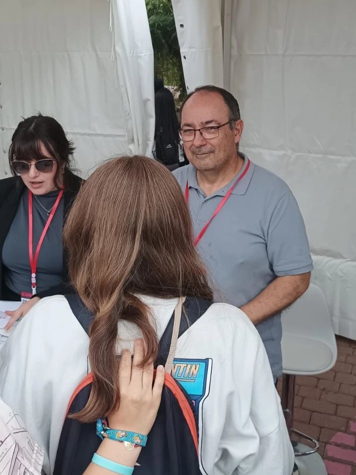 Una representante y un representante del Colegio, con acreditación roja, conversan con una estudiante en la carpa del CPCM.